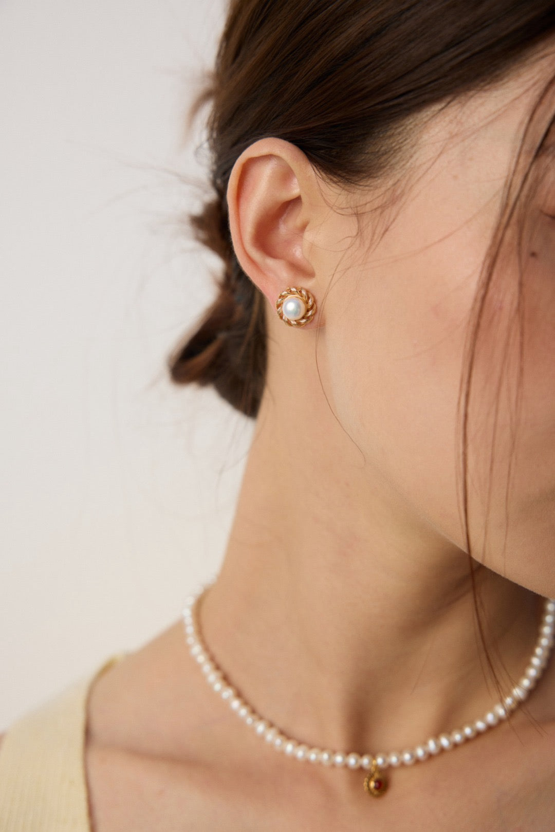 Close-up of a person wearing pearl earrings and a necklace against a neutral background