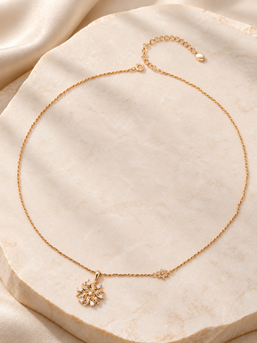 Elowen Radiant Bloom Pendant Necklace laid on pale stone, showing the floral pendant, small flower detail, and extender chain.