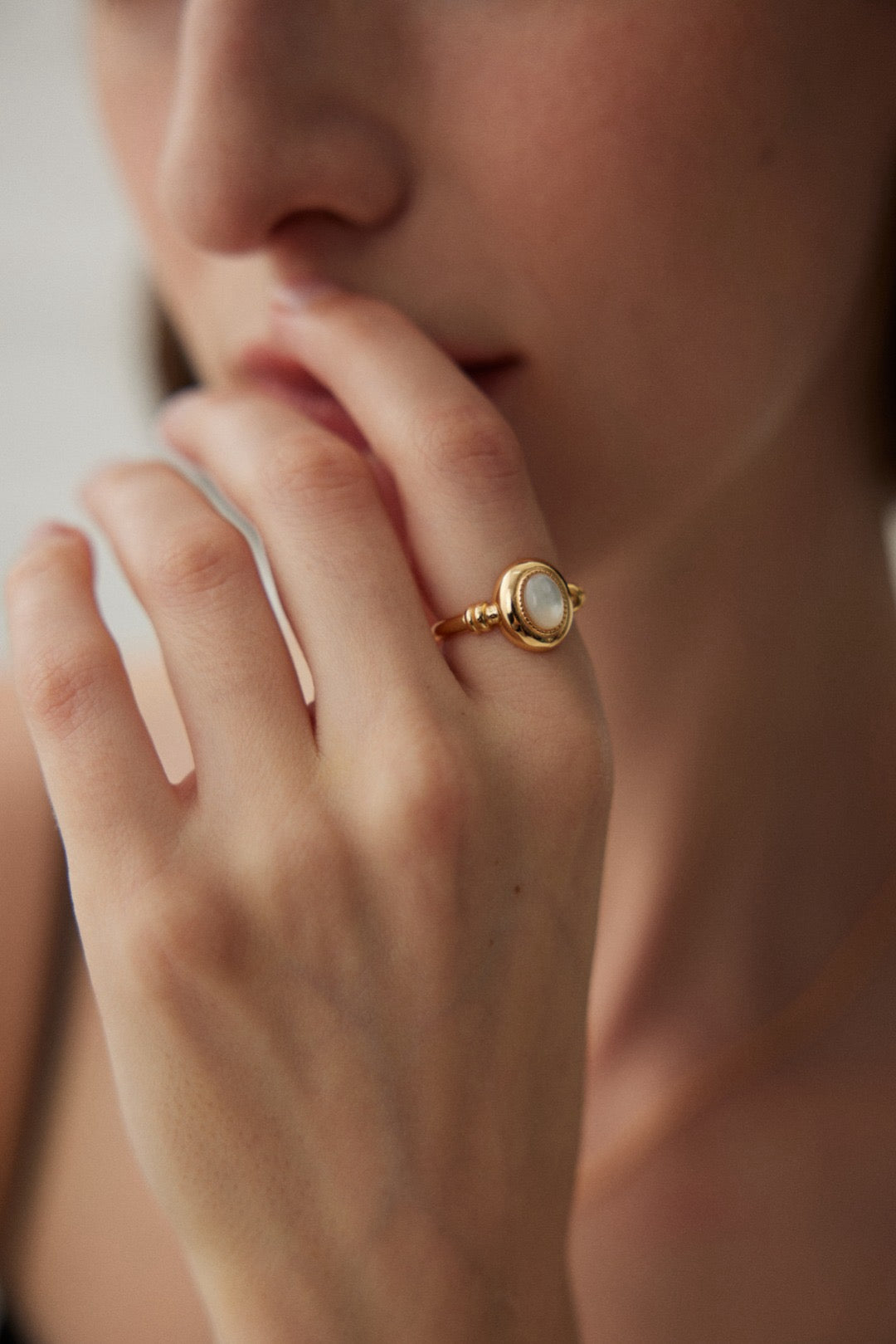 A person's hand with a gold-colored open band ring with a mother-of-pearl inlay.