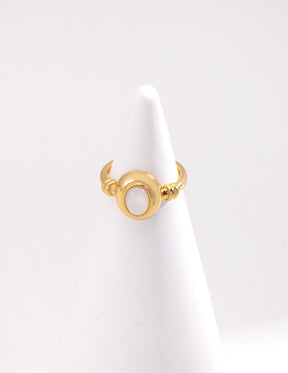 A gold-colored open band ring with a mother of pearl inlay displayed on the ring stand.