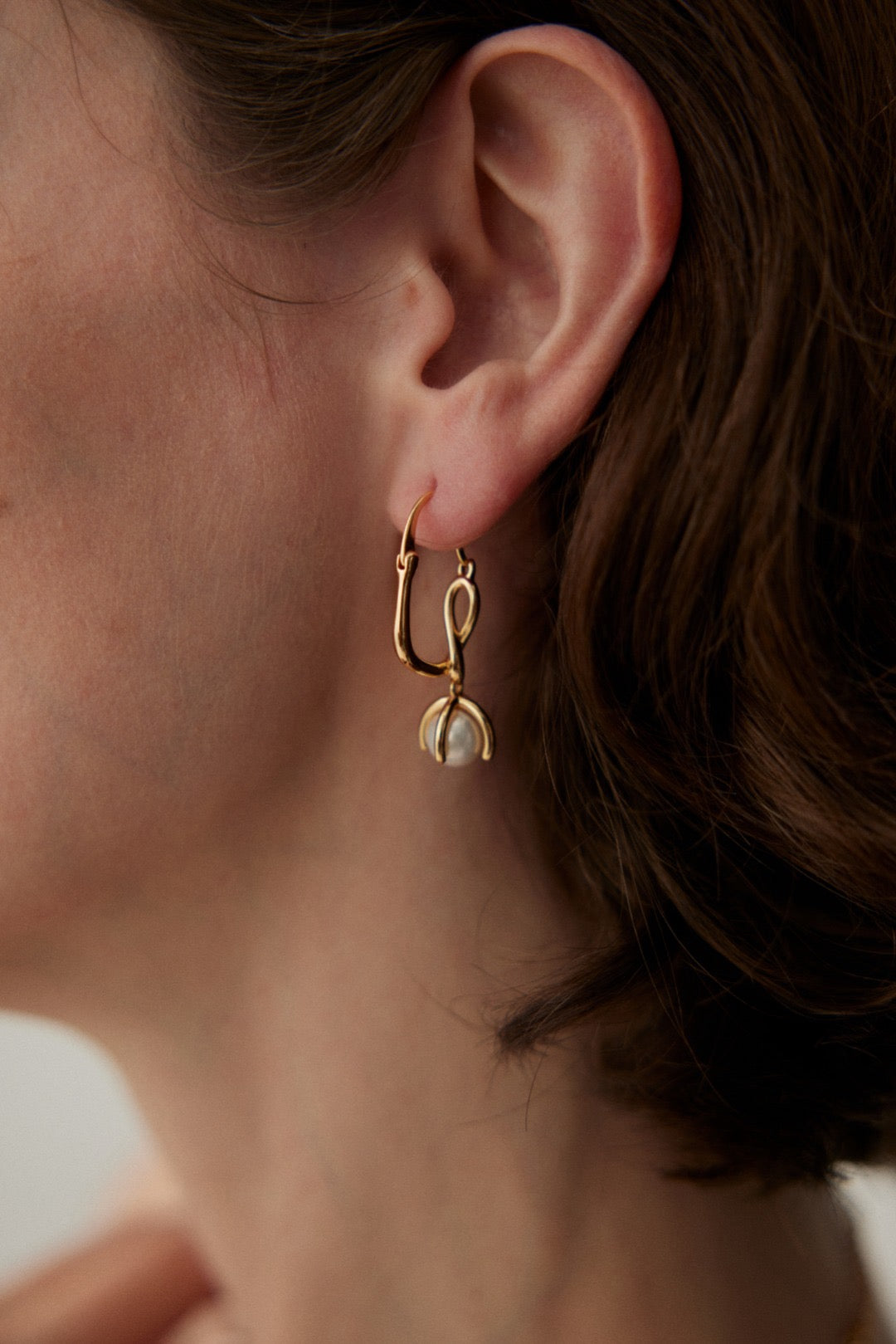 A close-up image of a woman's ear wearing a gold floral cage design drop earring with a lustrous pearl.