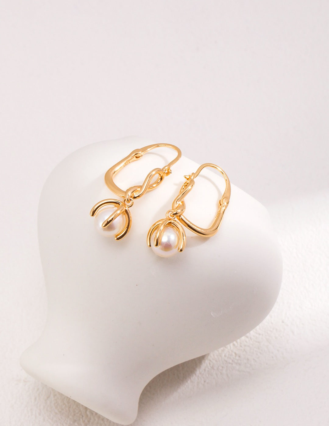 The Golden Bloom Pearl Earrings showcase lustrous 7.5mm freshwater pearls suspended from elegantly curved gold-toned hoops displayed on the white rock.