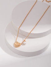 Gold heart-shaped pendant necklace with a pearl on a white background