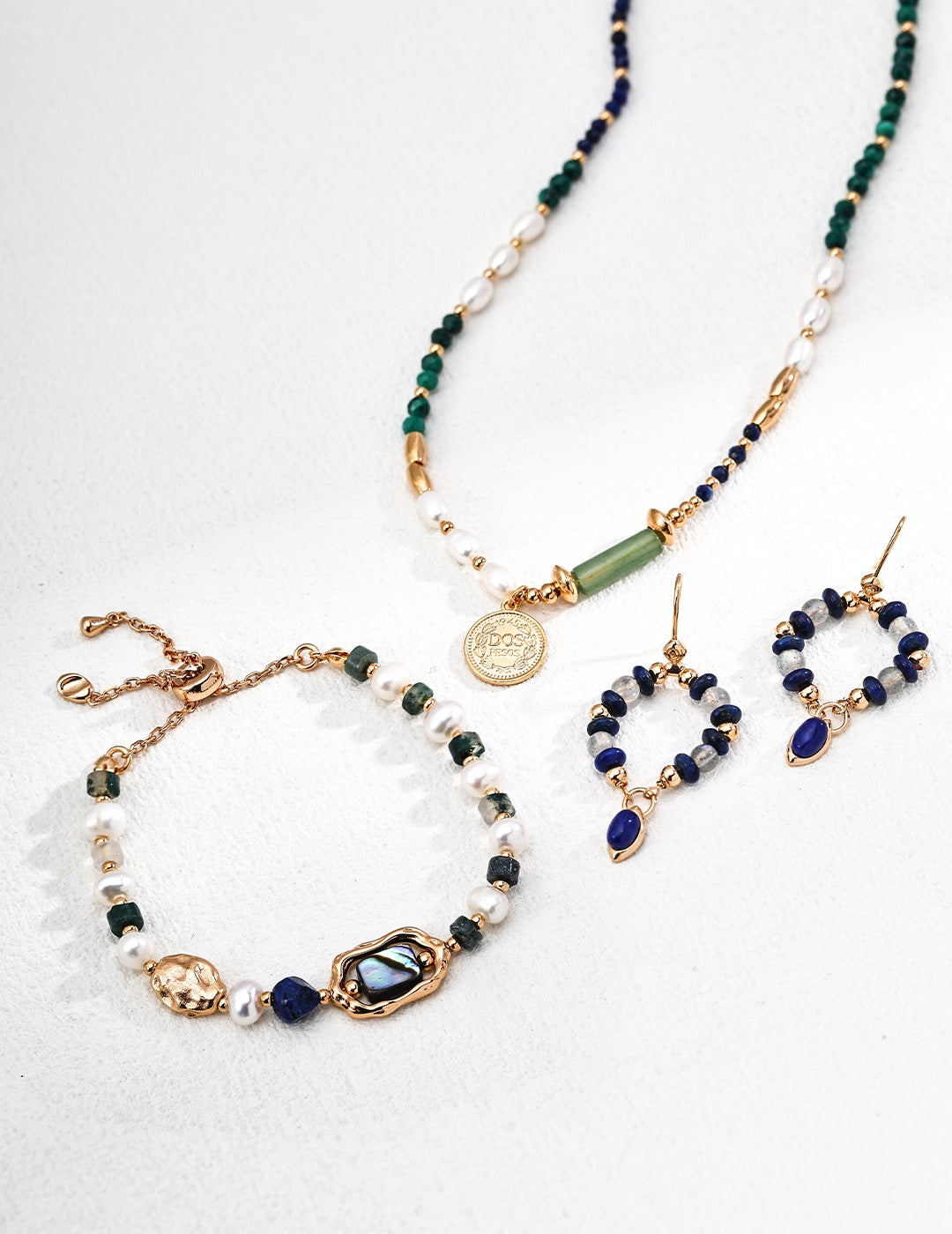 Set of jewelry including necklace, bracelet, and earrings with green and blue beads on a white background
