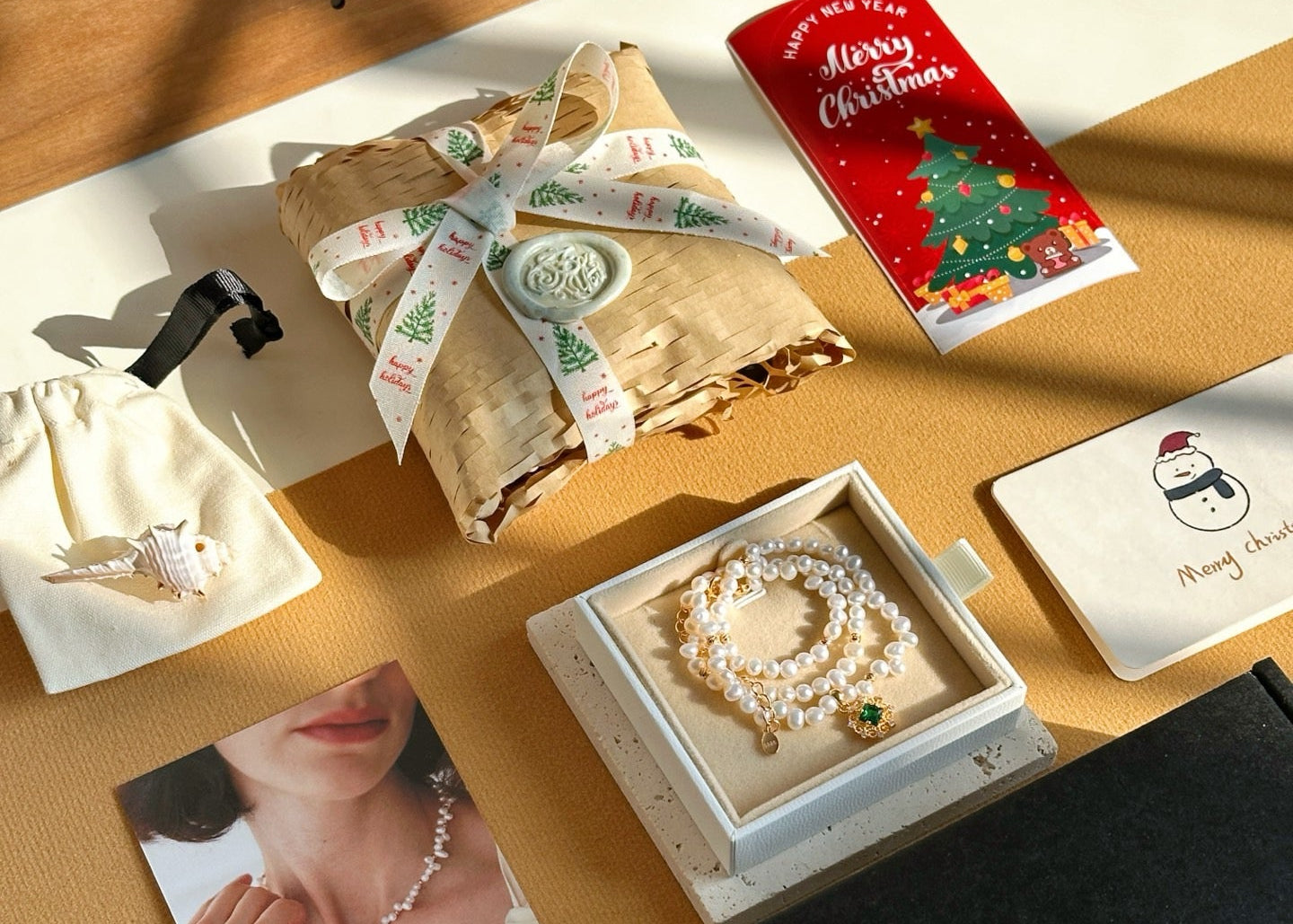 Jewelry set with a pearl necklace in a box, Christmas cards, and a photo of a woman wearing a pearl necklace on a wooden surface.
