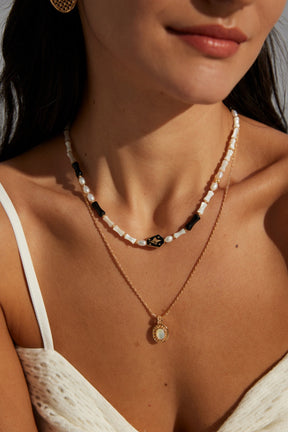 A person wearing a white strapless top, adorned with a gold vermeil necklace featuring a mother of pearl pendant.