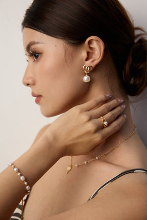 Woman wearing pearl jewelry including earrings, necklace, and bracelet against a neutral background