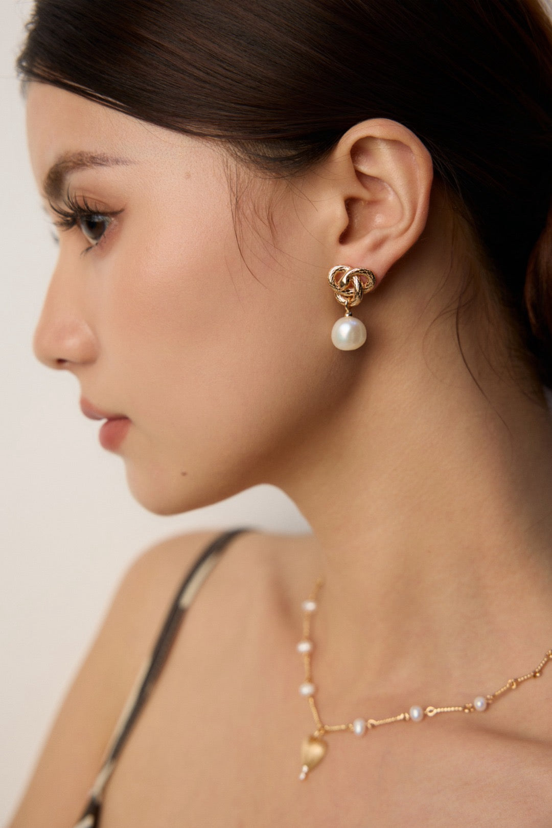 Woman wearing gold knot earrings with pearls against a neutral background