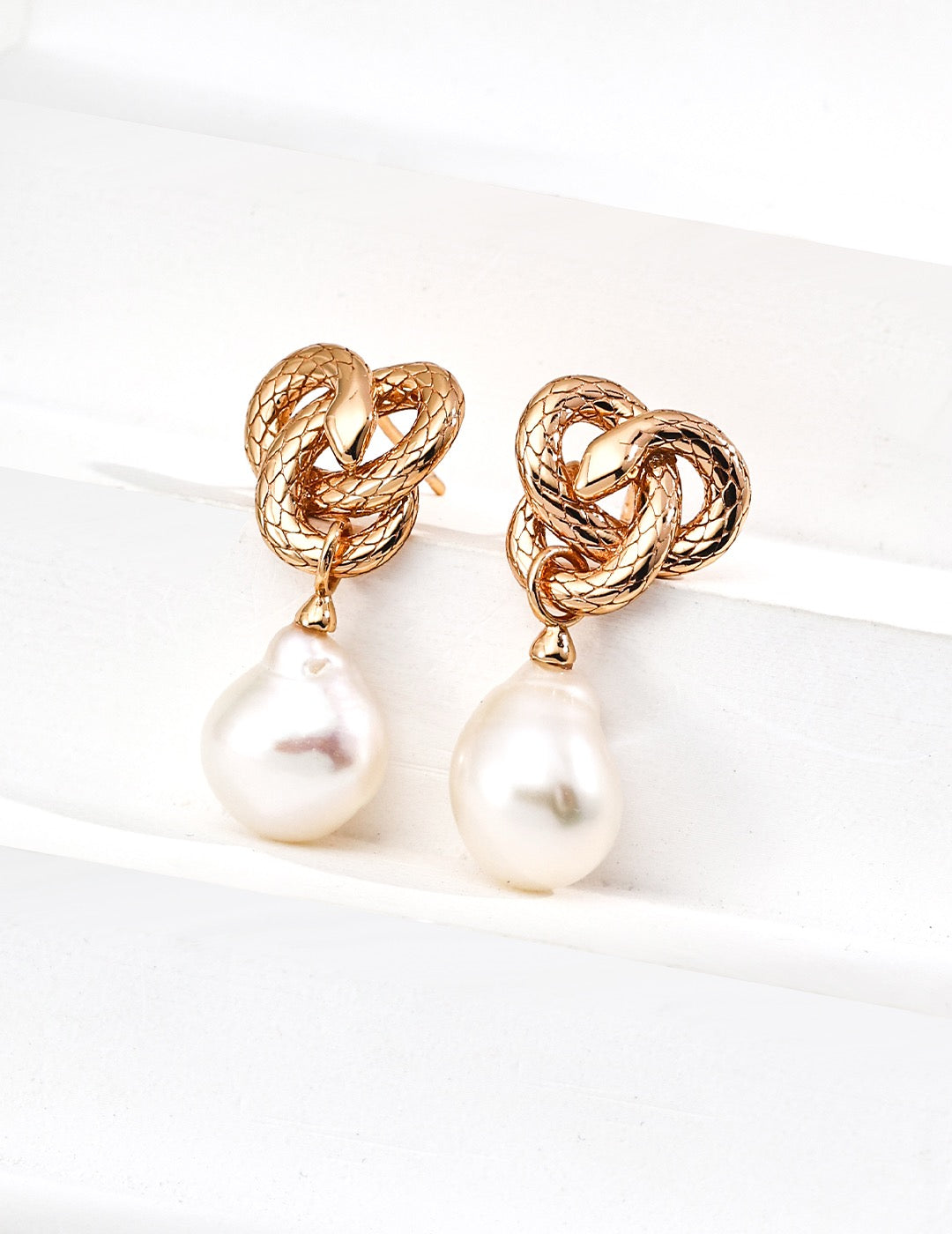 Gold knotted earrings with pearl drops on a white background