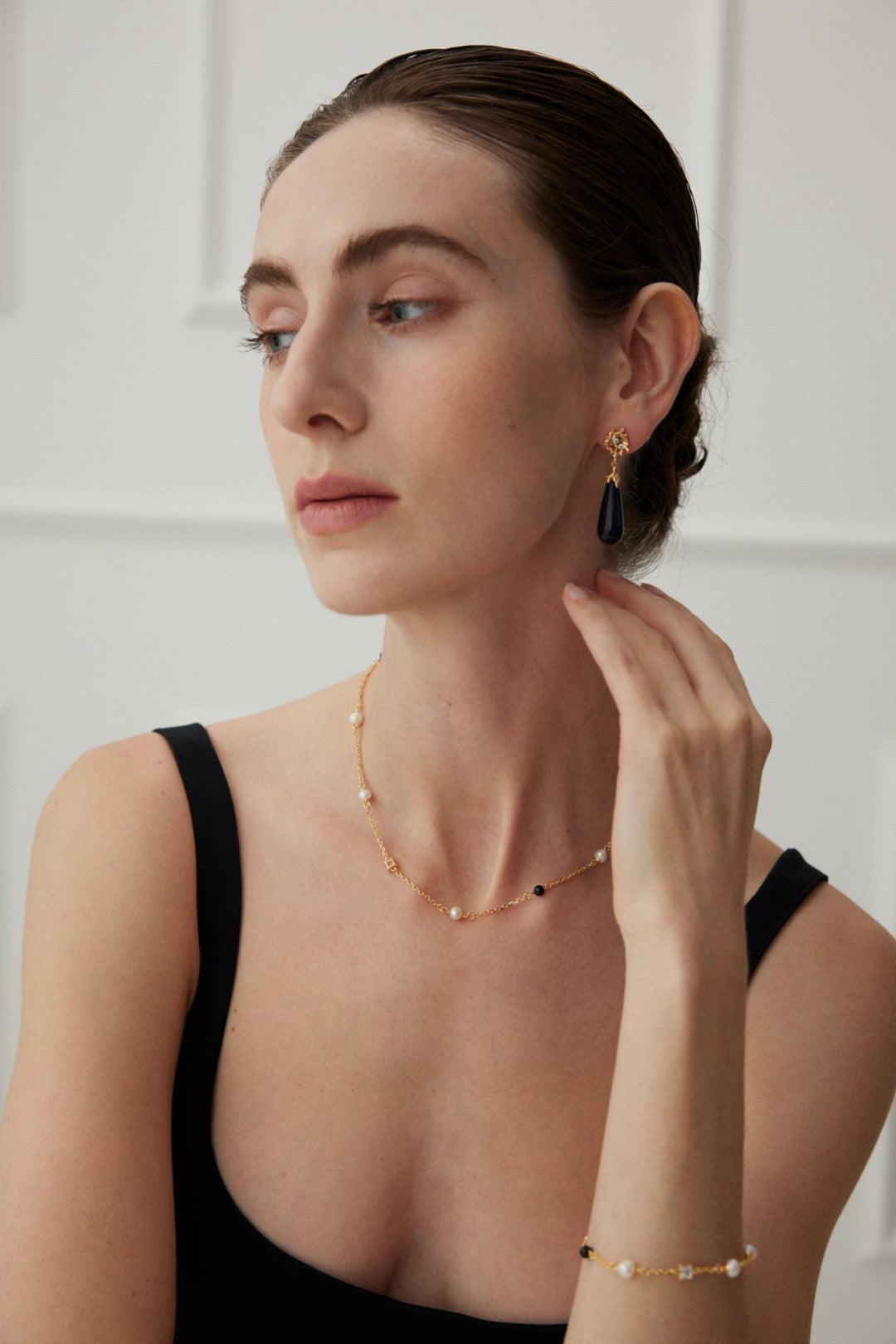 The model wears the Isla Necklace and Bracelet in 18K Gold Freshwater Pearl Zircon Black Agate.