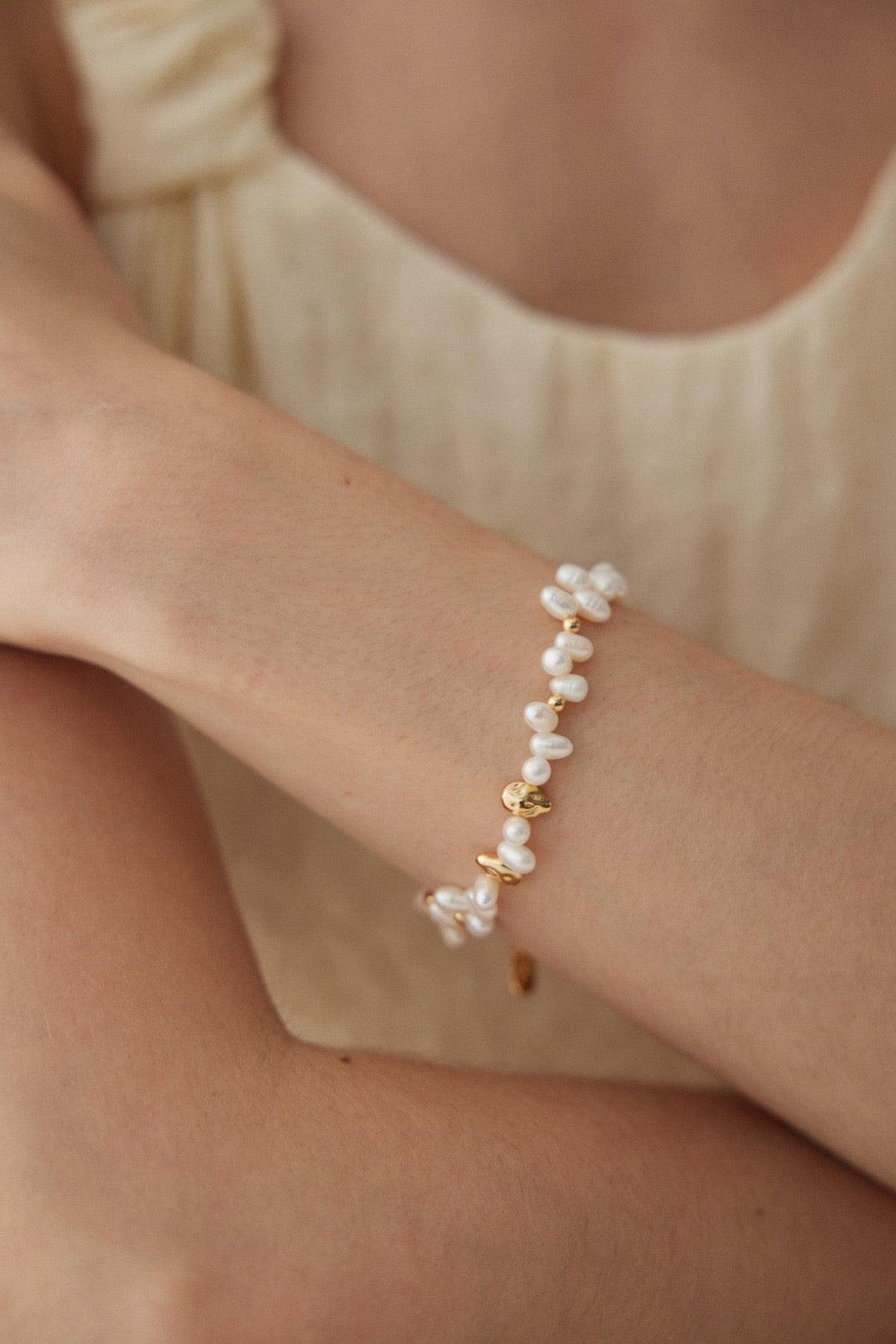 A person wearing a beige dress, showcasing a gold vermeil bracelet with white pearls on their wrist.