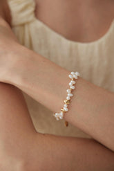 A person wearing a beige dress, showcasing a gold vermeil bracelet with white pearls on their wrist.