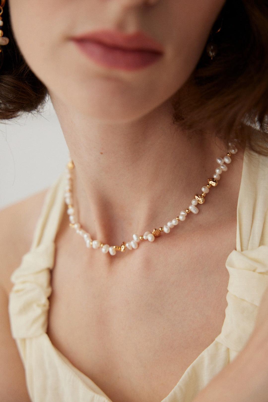 A close-up of a person wearing a white garment with a gold and pearl necklace.
