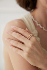 A person wearing a ring with a gold band and a white shell pearl on their finger.