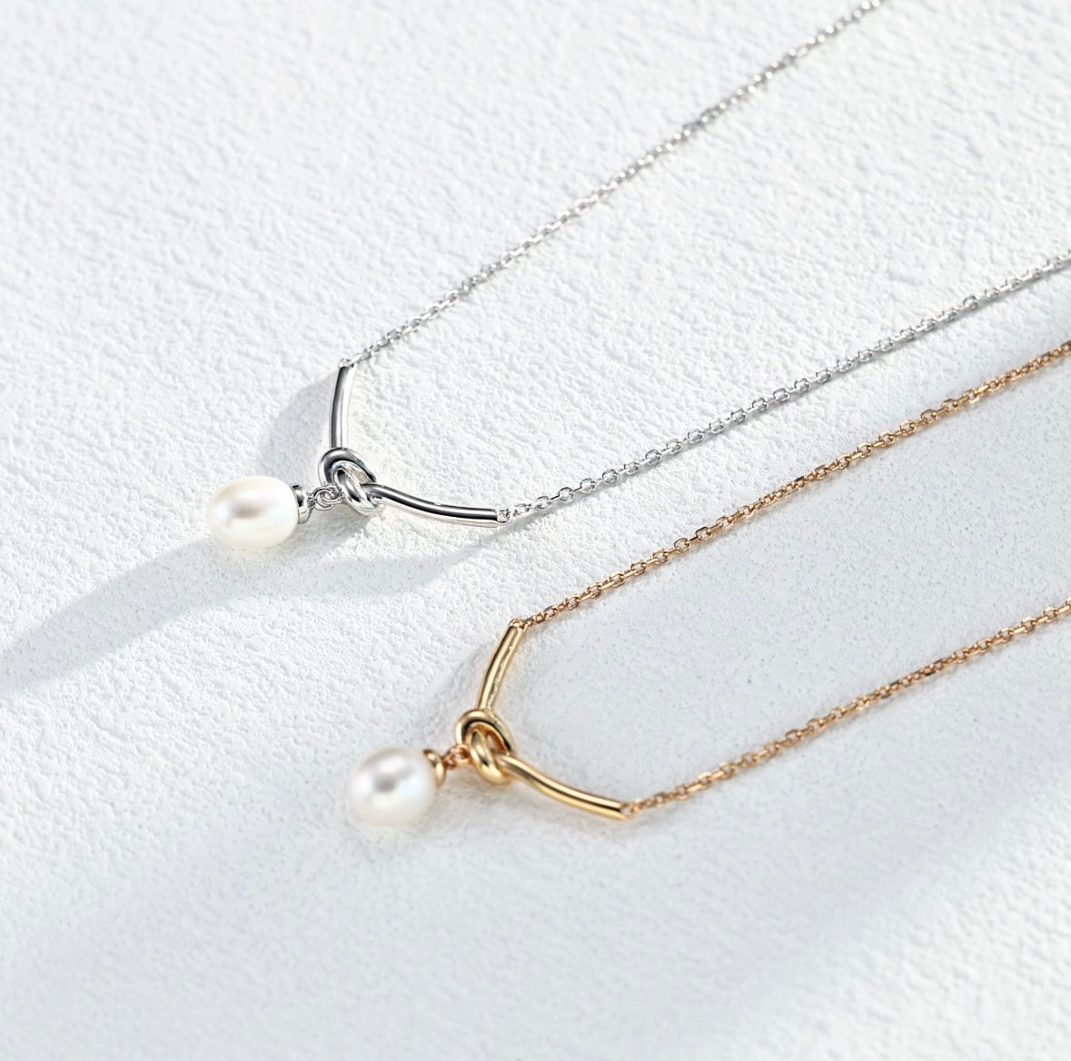 Two pearl necklaces, one gold and one silver, on a white background.