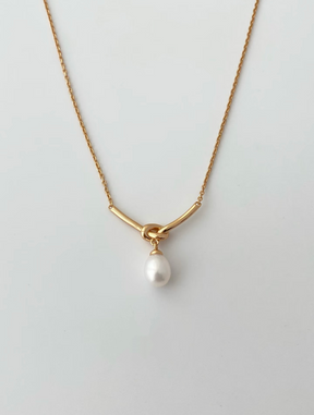 Gold necklace with a single pearl pendant on a light gray background