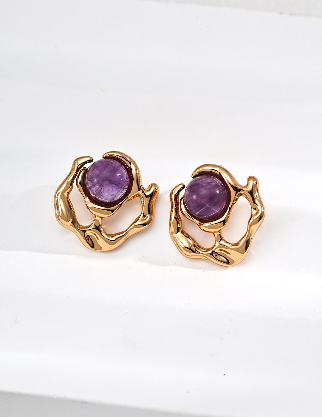 Pair of gold earrings with purple gemstones on a white background