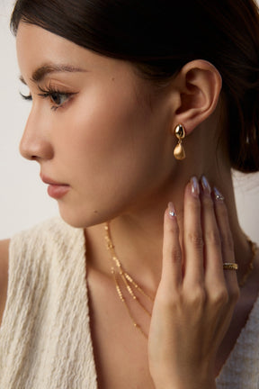 Woman wearing gold earrings and necklaces with a neutral background