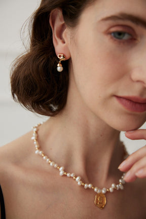 A close-up of a woman wearing a gold vermeil earring with a hexagonal stud and a dangling freshwater pearl.