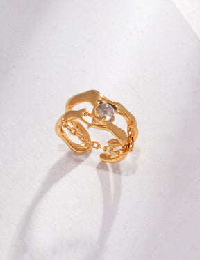 Gold and silver adjustable rings with sculpted, wave-like design and a raw labradorite stone drop, displayed on a minimalist white surface.