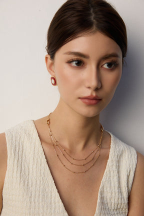 Woman wearing gold necklaces and earrings against a plain background