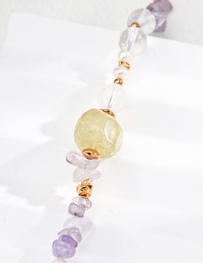 Close-up of an amethyst, rose quartz, and freshwater pearls bracelet with a citrine on a white background.
