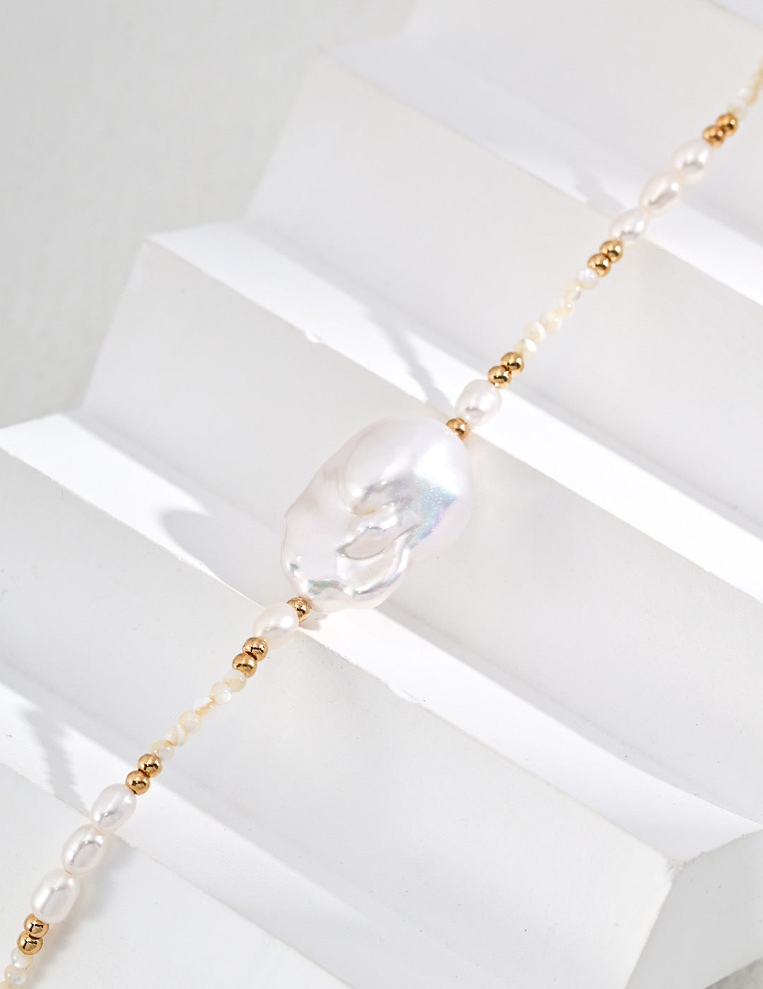 Close up of the large baroque pearl pendant necklace with gold beads and freshwater pearls displayed on the withe stage. 