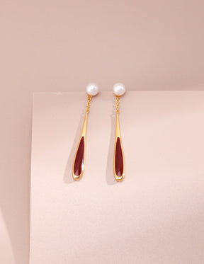 Pair of earrings with gold and red design on a light pink background