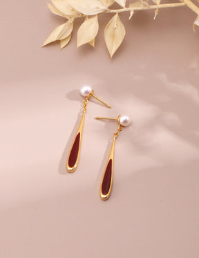 Gold earrings with red accents on a beige background