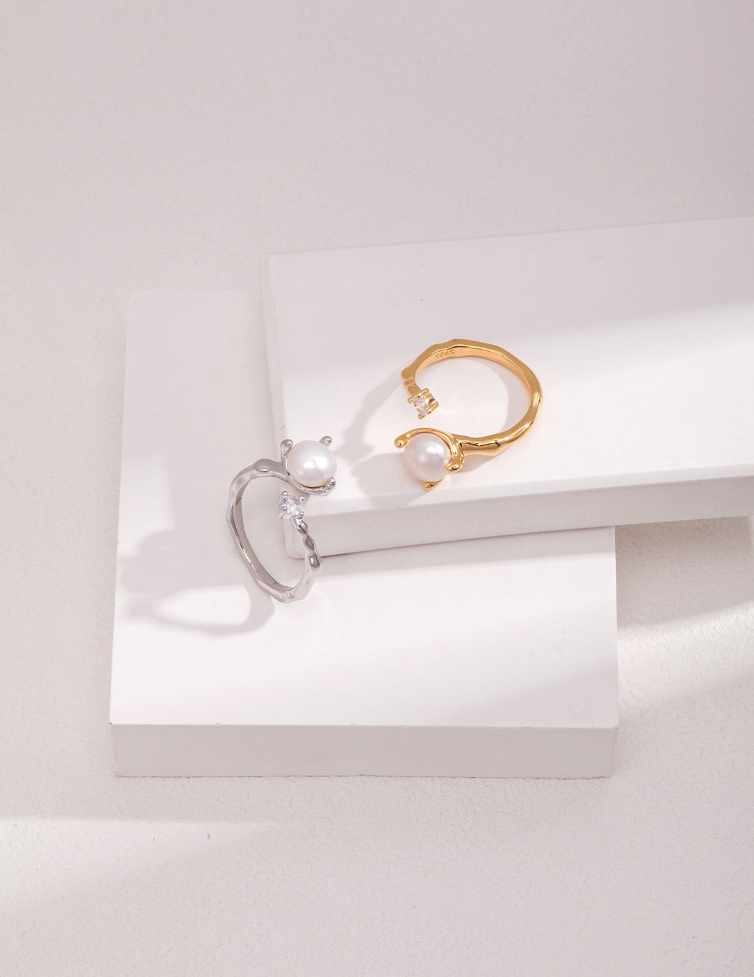 Two stackable open rings, silver and gold, with an 8mm pearl and zircon displayed on the white rocks.