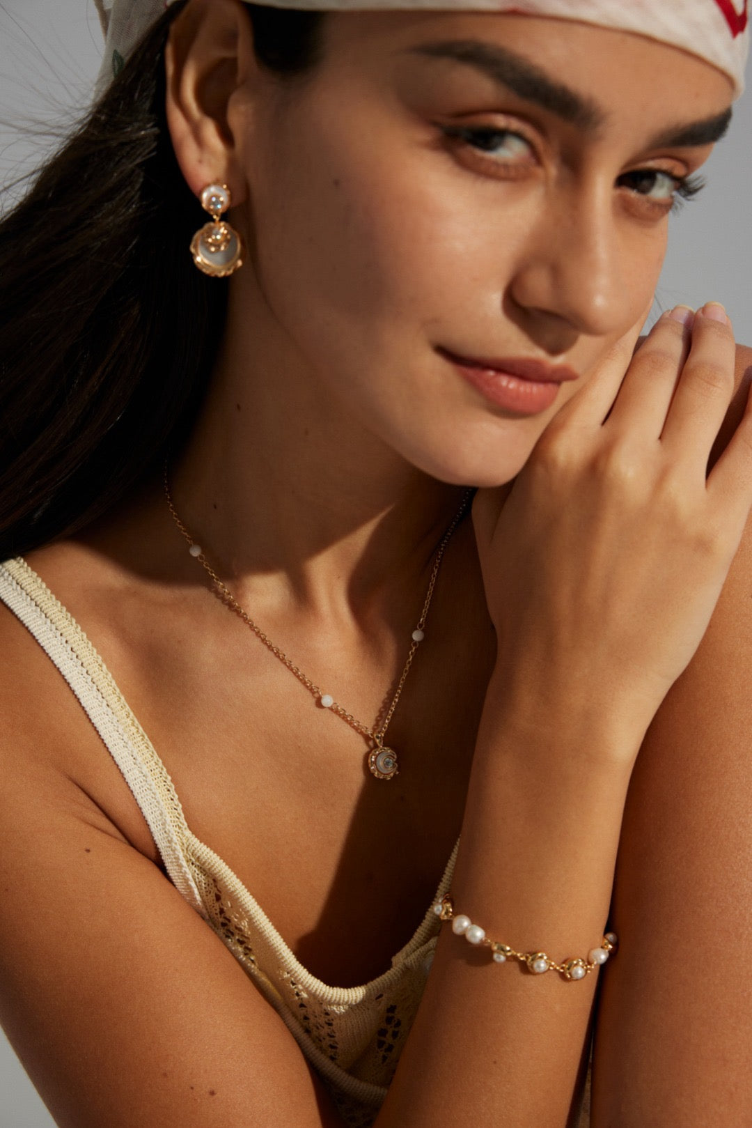 A woman showcasing the Rayna Necklace, which is silver with gold vermeil accents, and features mother of pearl and zircon stones. She is also wearing matching earrings and a bracelet.