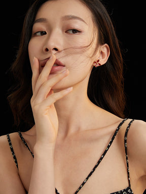 A woman wearing a black strappy top and red enamel daisy stud earrings with a blurred background