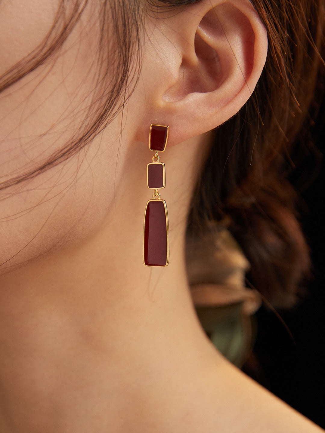 Close-up of an ear wearing a gold earring with red stones.