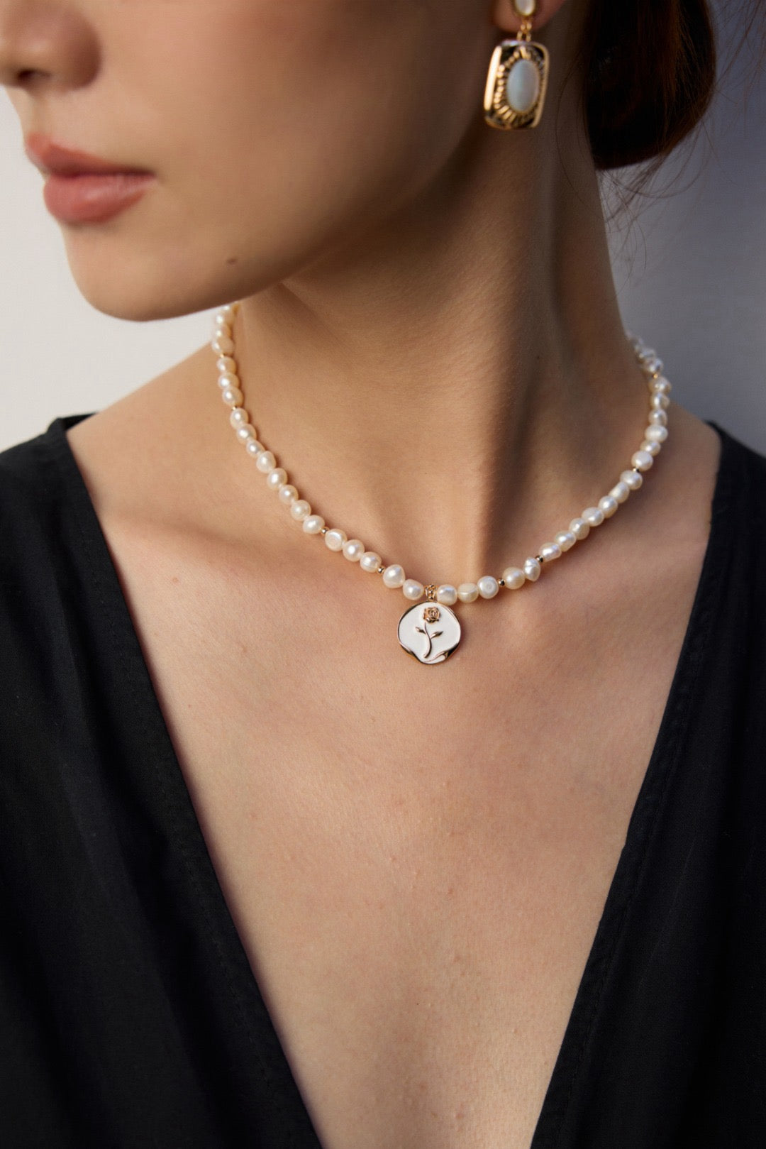 Pearl necklace with a gold pendant worn by a person against a neutral background