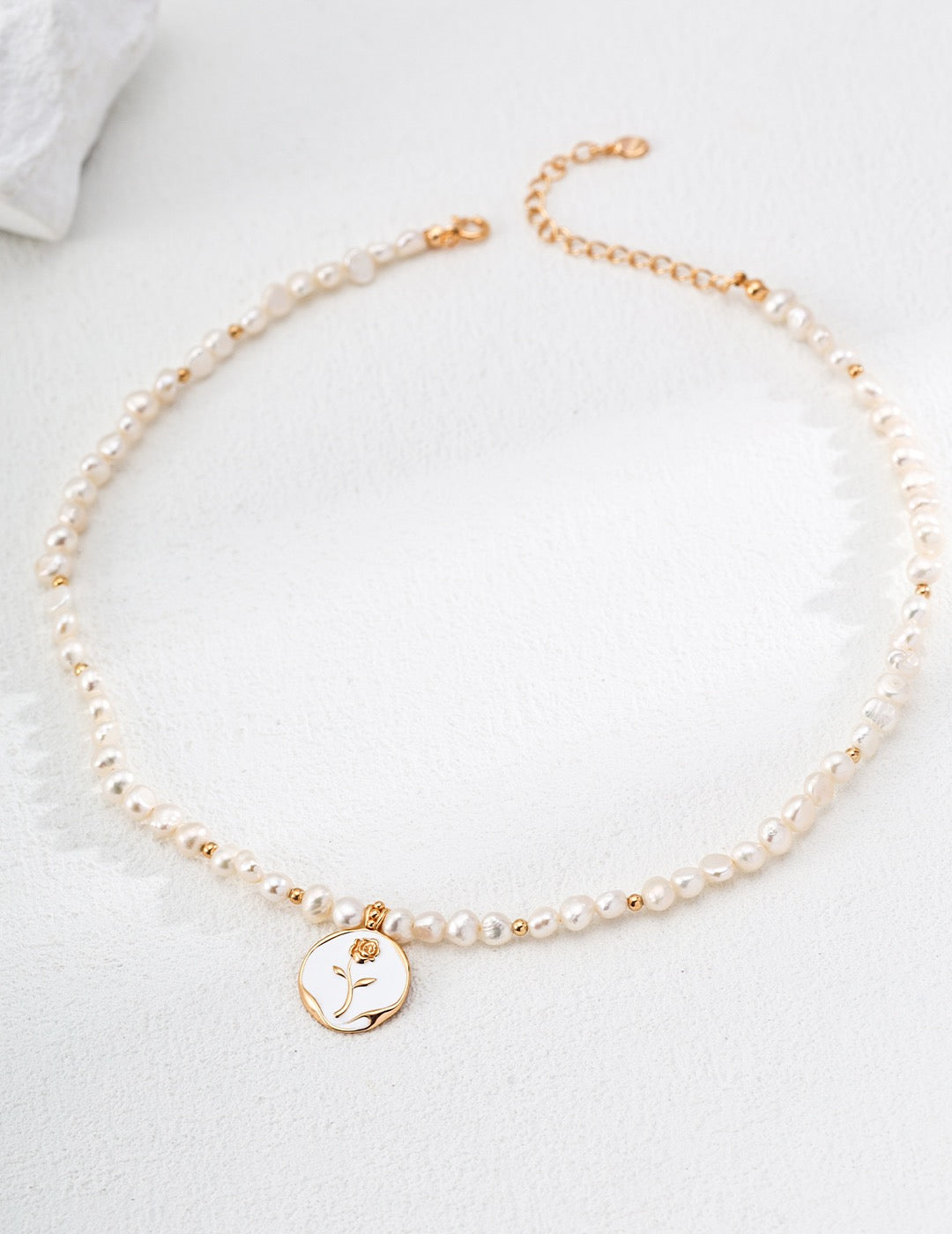 Pearl necklace with a gold hand-painted rosecharm on a white background