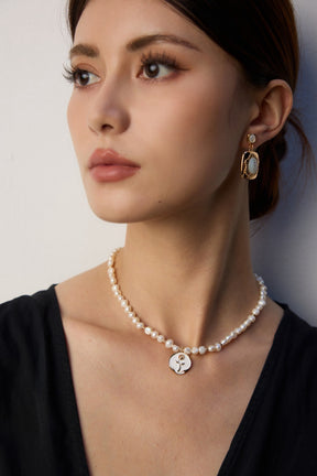 Woman wearing a pearl necklace and earrings against a neutral background