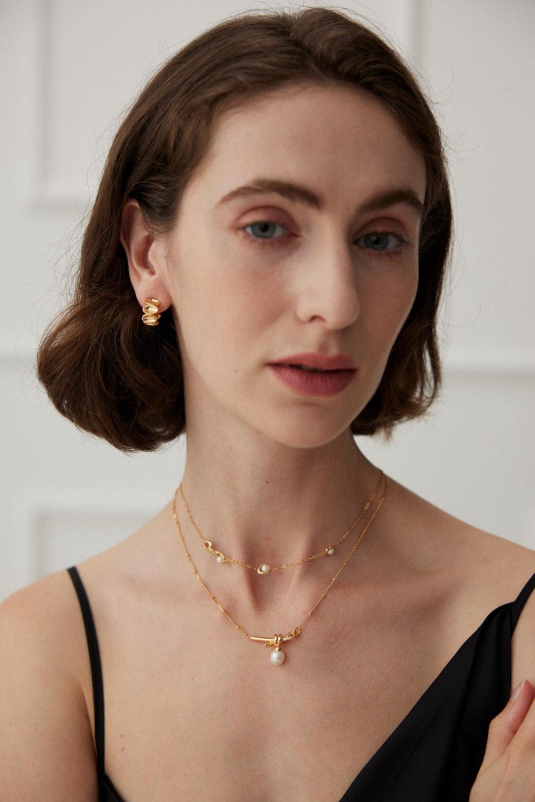 A person wearing a black tank top and showcasing a gold vermeil necklace with a fresh water pearl pendant and a bow knot design.