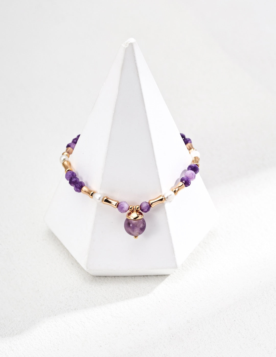 Necklace with purple and gold beads on a white stand against a white background