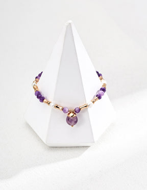 Necklace with purple and gold beads on a white stand against a white background