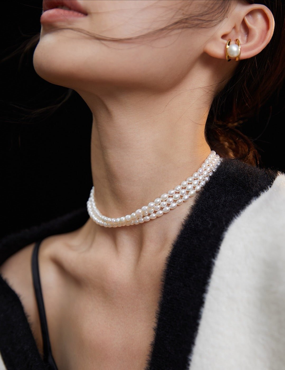 Close-up of a person wearing a pearl necklace and earring against a black background