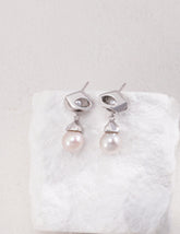 The Silver Luna Pearl Drop Earrings hanged on the white rock.