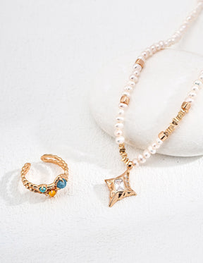 Gold ring with gemstones and a pearl necklace on a white surface