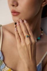 Close-up of a woman's hand with rings, wearing a colorful top against a neutral background