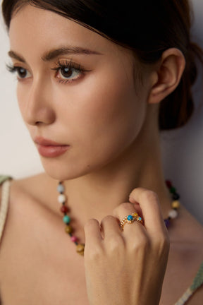 Woman wearing colorful jewelry including a necklace and ring, with a neutral background