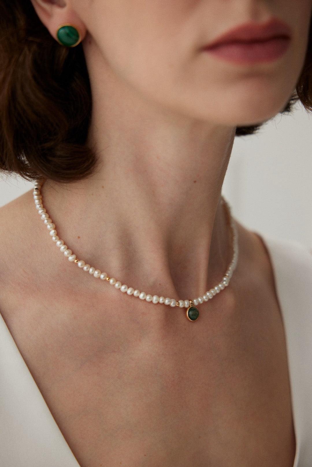 A person wearing a Tessa Malachite Necklace, which is composed of white pearls and a green gemstone pendant.