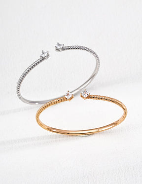 Elegant twisted open cuff bracelet in sterling silver and gold vermeil with zircon accents, styled on a minimal white background.