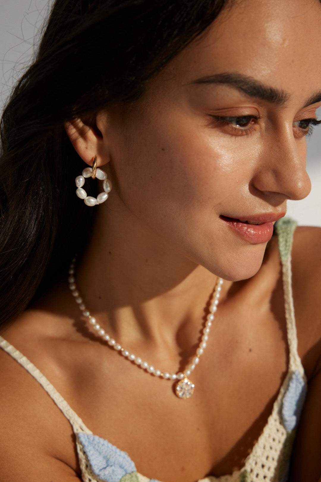 A woman wearing a necklace with twisted hoop earrings and freshwater pearl clusters.