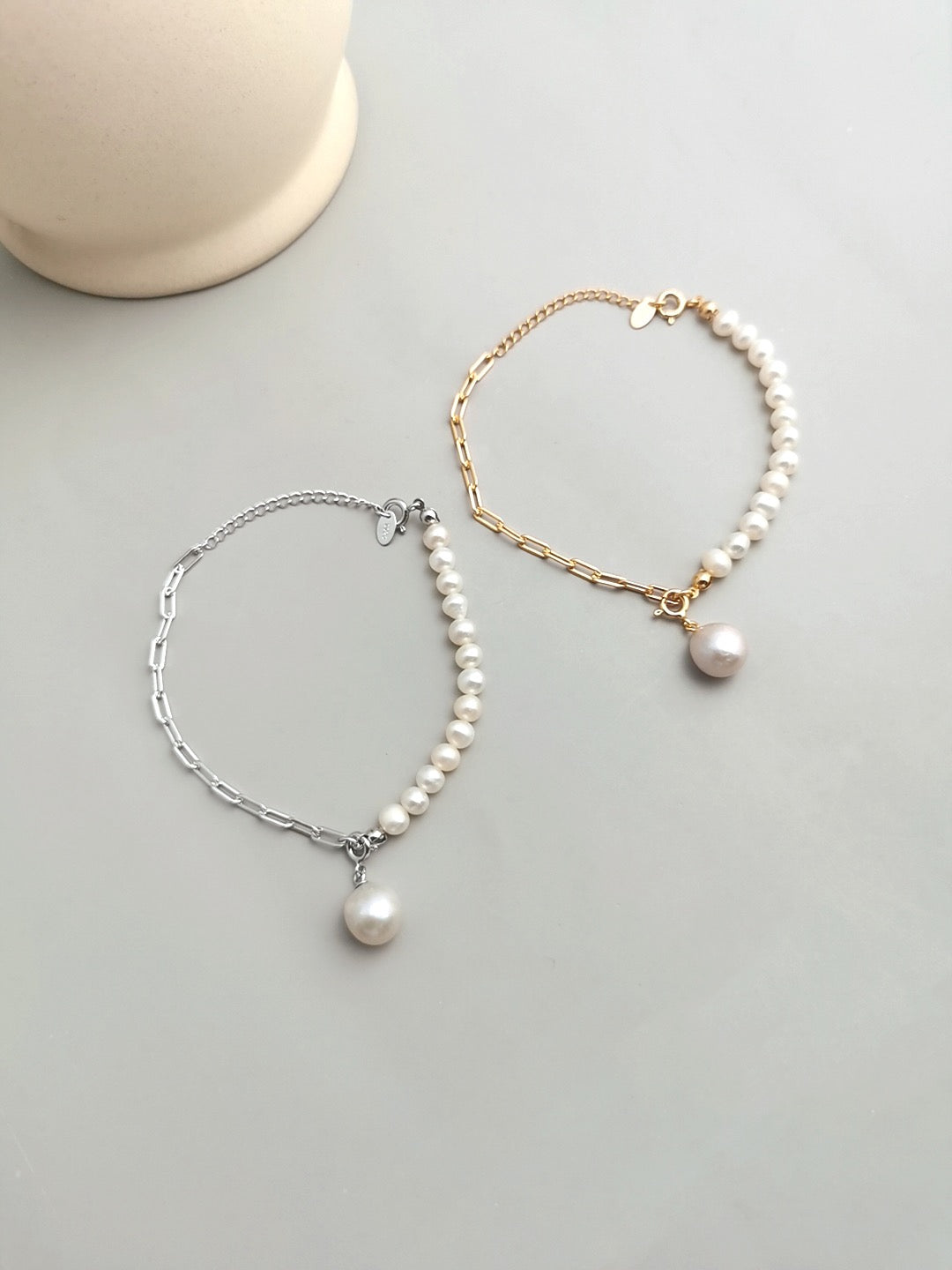 Two Luna Dual-Chain Freshwater Pearl Bracelets, featuring a combination of a delicate pearl strand and a sleek metal chain, with a single pearl charm. One bracelet is gold-toned, and the other is silver-toned, displayed on a light, minimalist background.