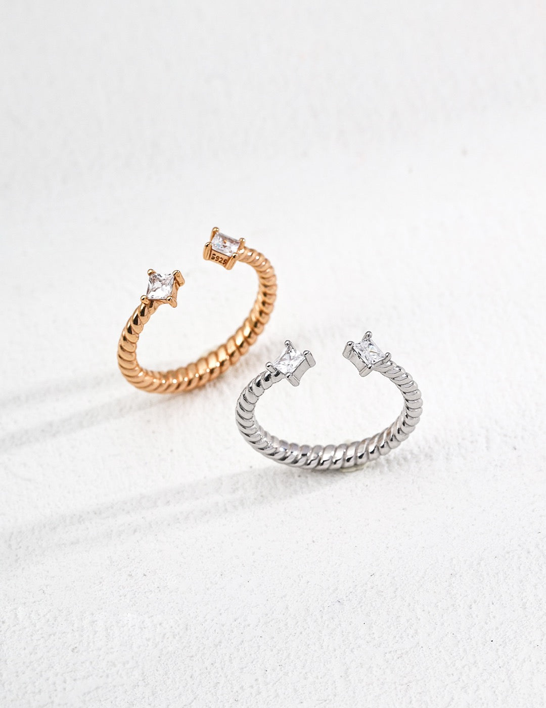 Two Twilight Twist Open Rings in gold and silver with twisted band design and zircon stone ends, displayed on a white background.