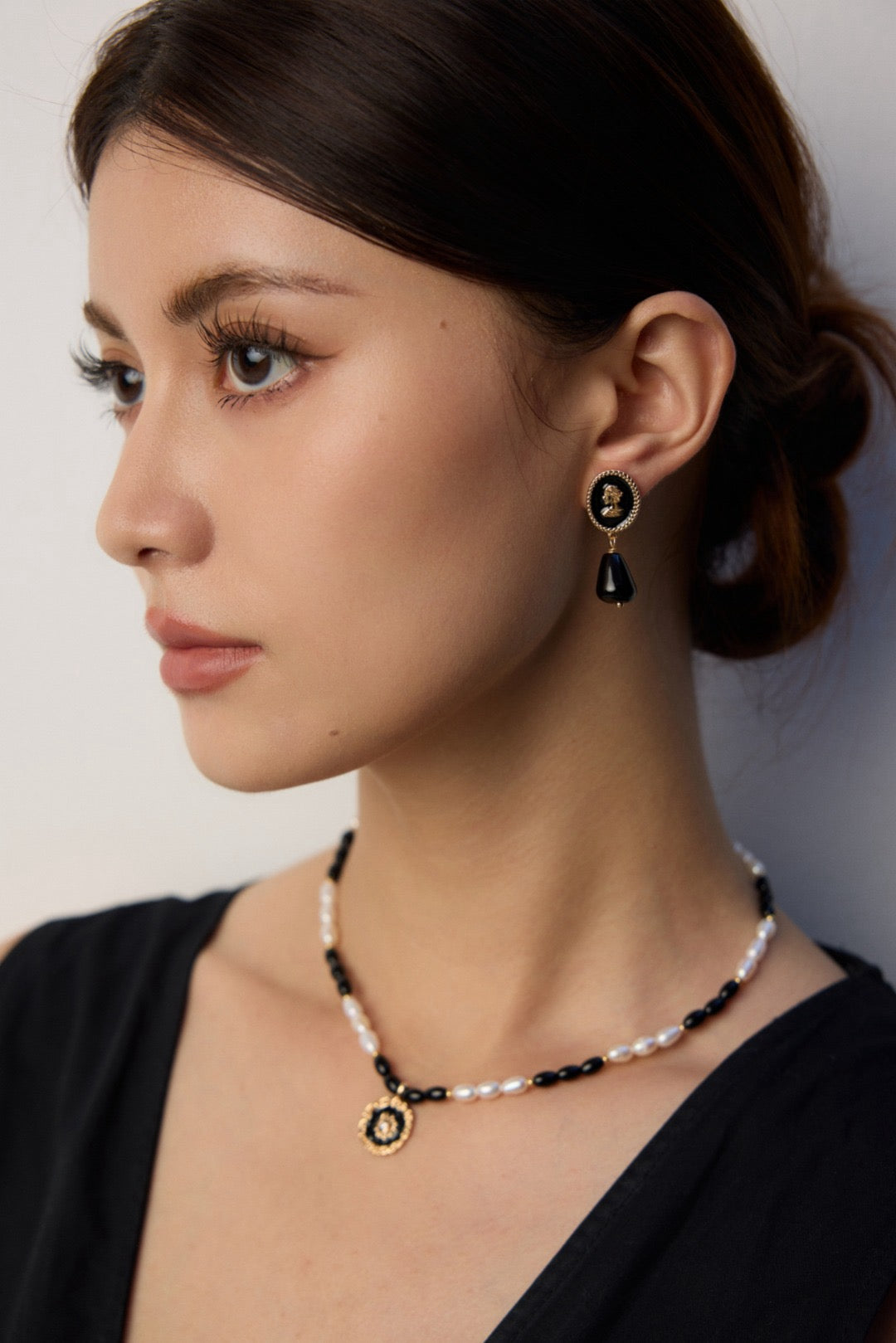 Woman wearing black and gold earrings and necklace against a neutral background
